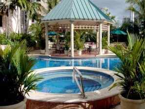Una piscina con un pabellón, palmeras y un paisaje urbano de fondo.