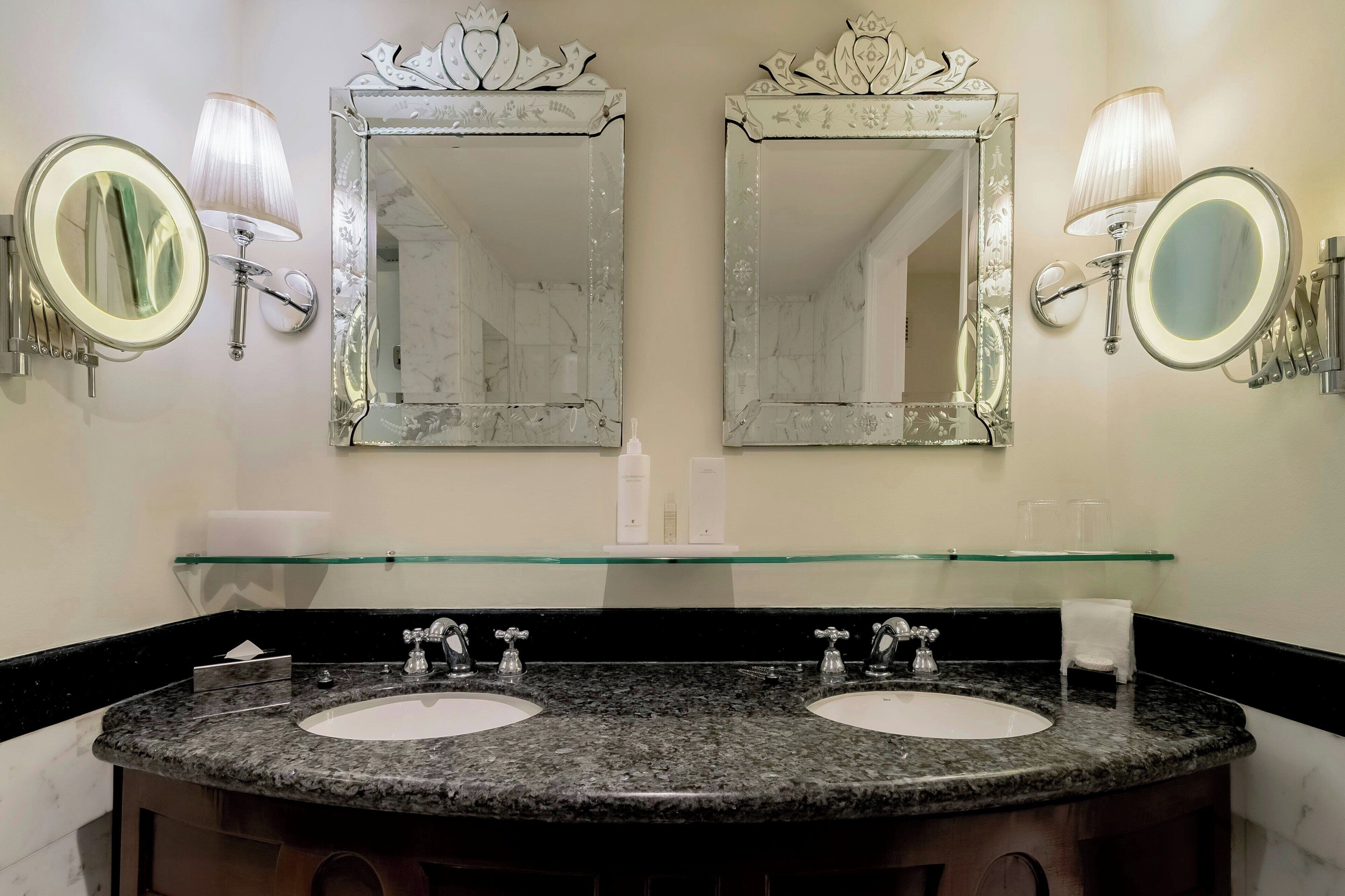 A bathroom with two sinks, a glass shelf, and two wall-mounted mirrors with decorative frames.