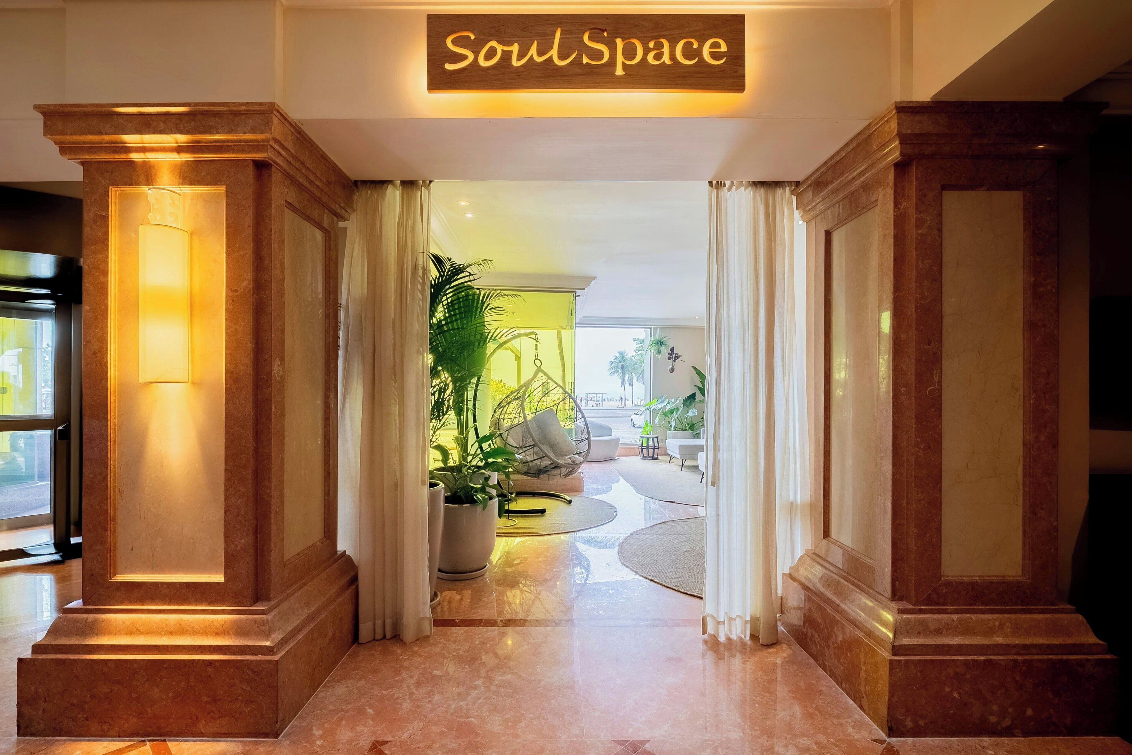 A hotel lobby with a sign reading "SoulSpace," marble columns, a potted plant, and a seating area with a round rug.
