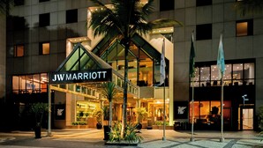 Hotel JW Marriott con fachada de vidrio moderna, palmeras y una entrada bien iluminada.