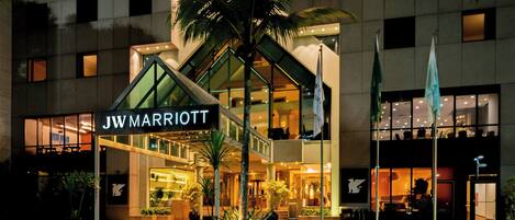Hotel JW Marriott con fachada de vidrio moderna, palmeras y una entrada bien iluminada.