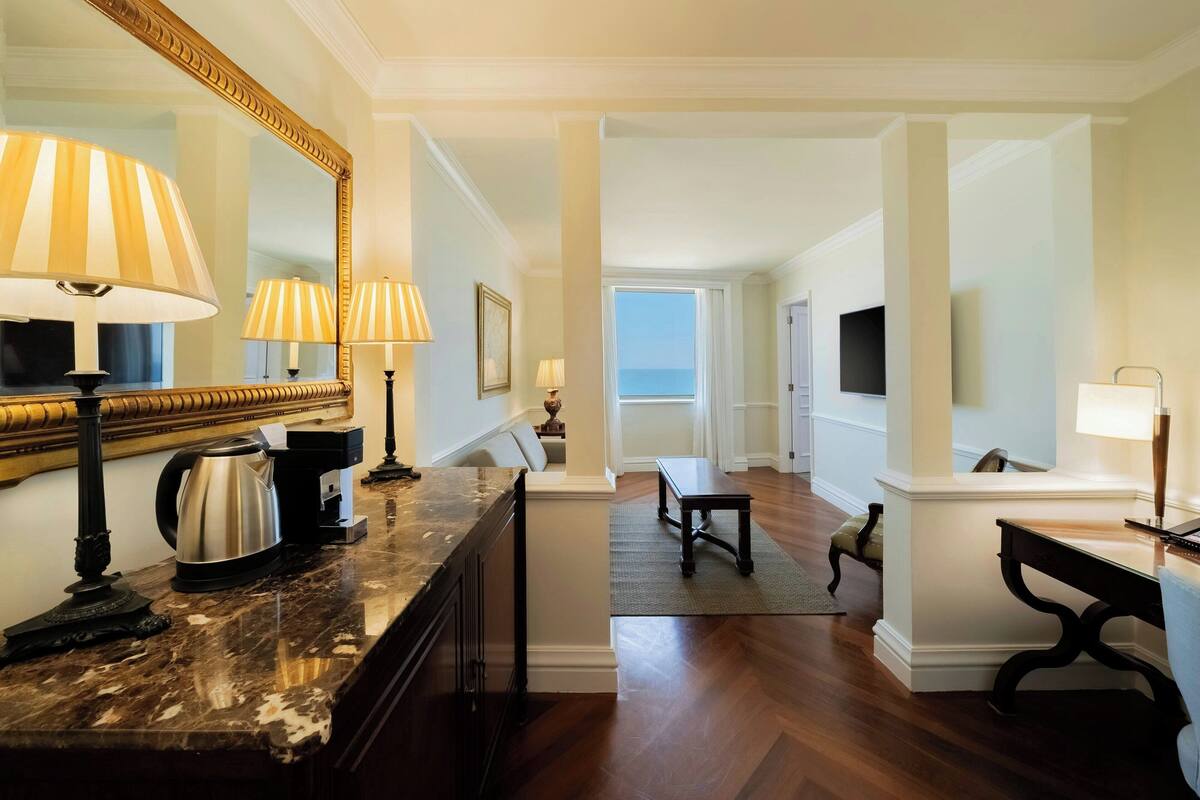 A hotel room with a marble countertop, a coffee maker, a lamp, a television, and a view of the ocean.