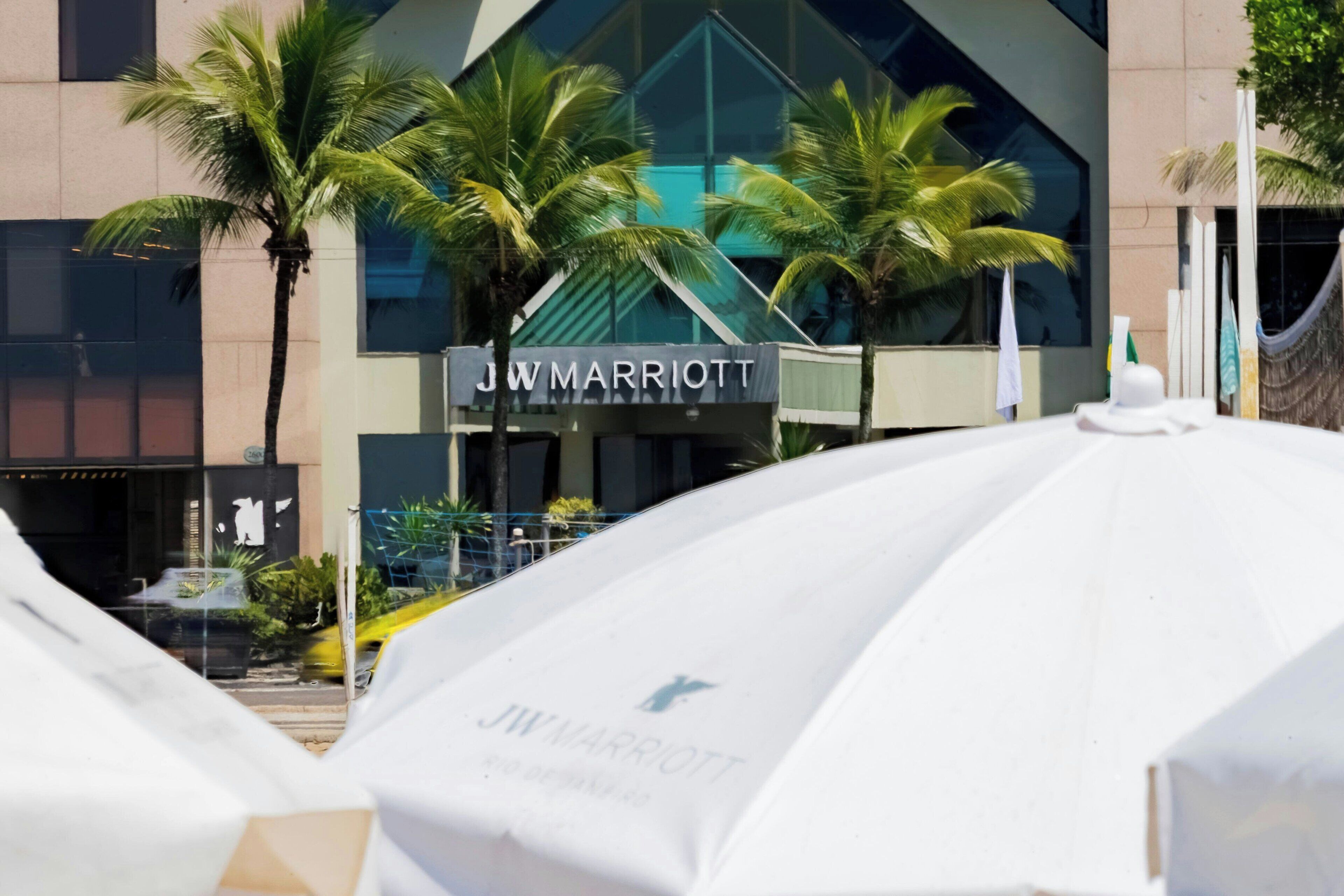 Un hôtel JW Marriott doté d’une façade moderne en verre, de palmiers et d’un espace extérieur aménagé avec des sièges.