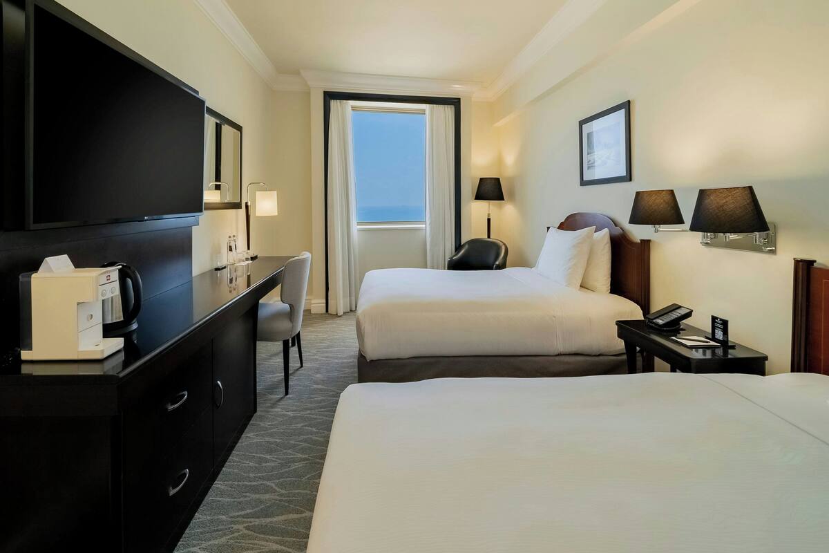 A hotel room with two beds, a desk with a coffee maker, a TV, and a window with a view.