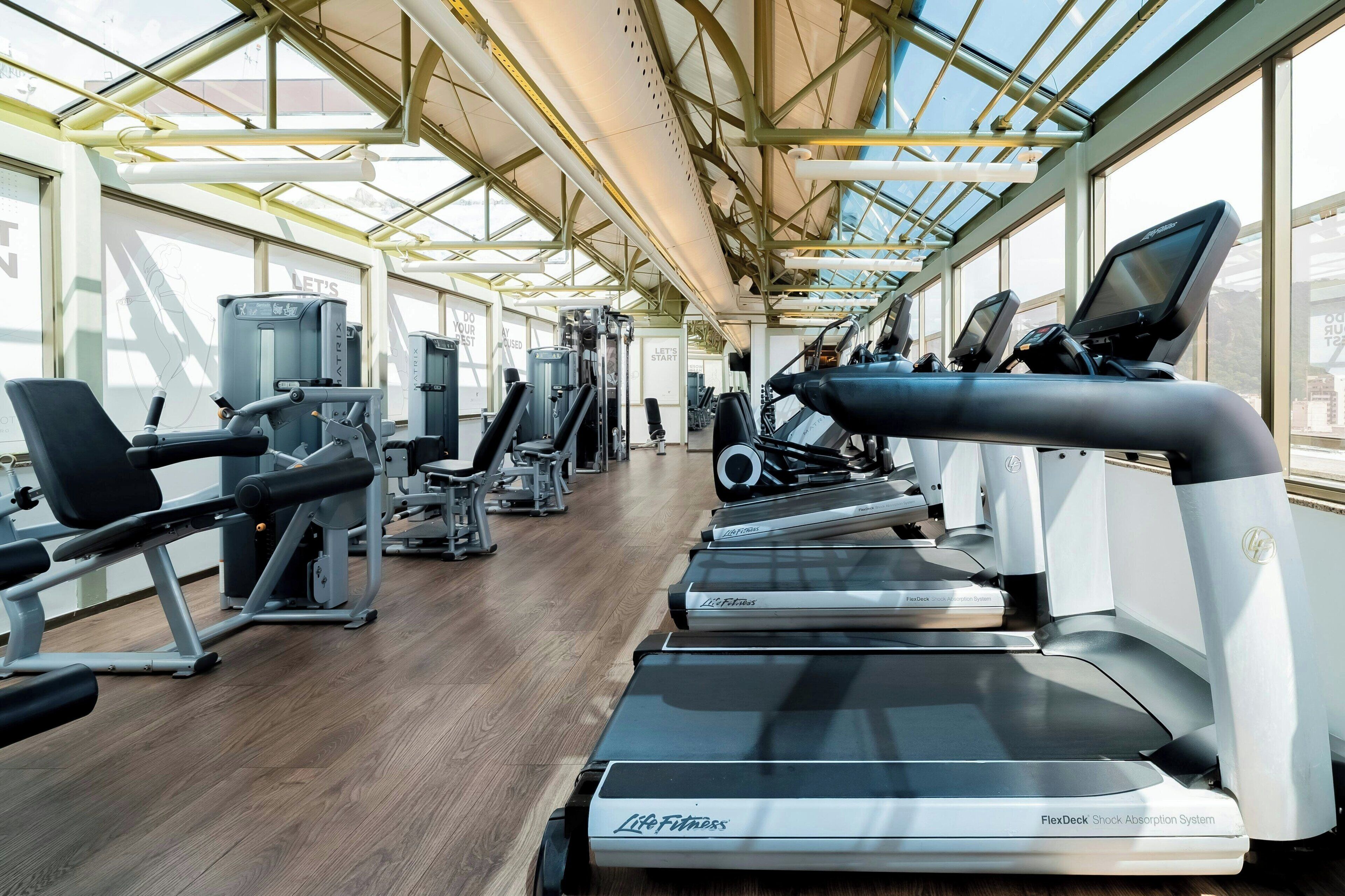 A gym with treadmills, weight machines, and exercise equipment under a large glass ceiling.