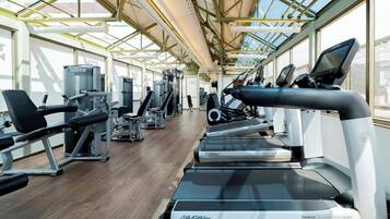 A gym with treadmills, weight machines, and exercise equipment under a large glass ceiling.