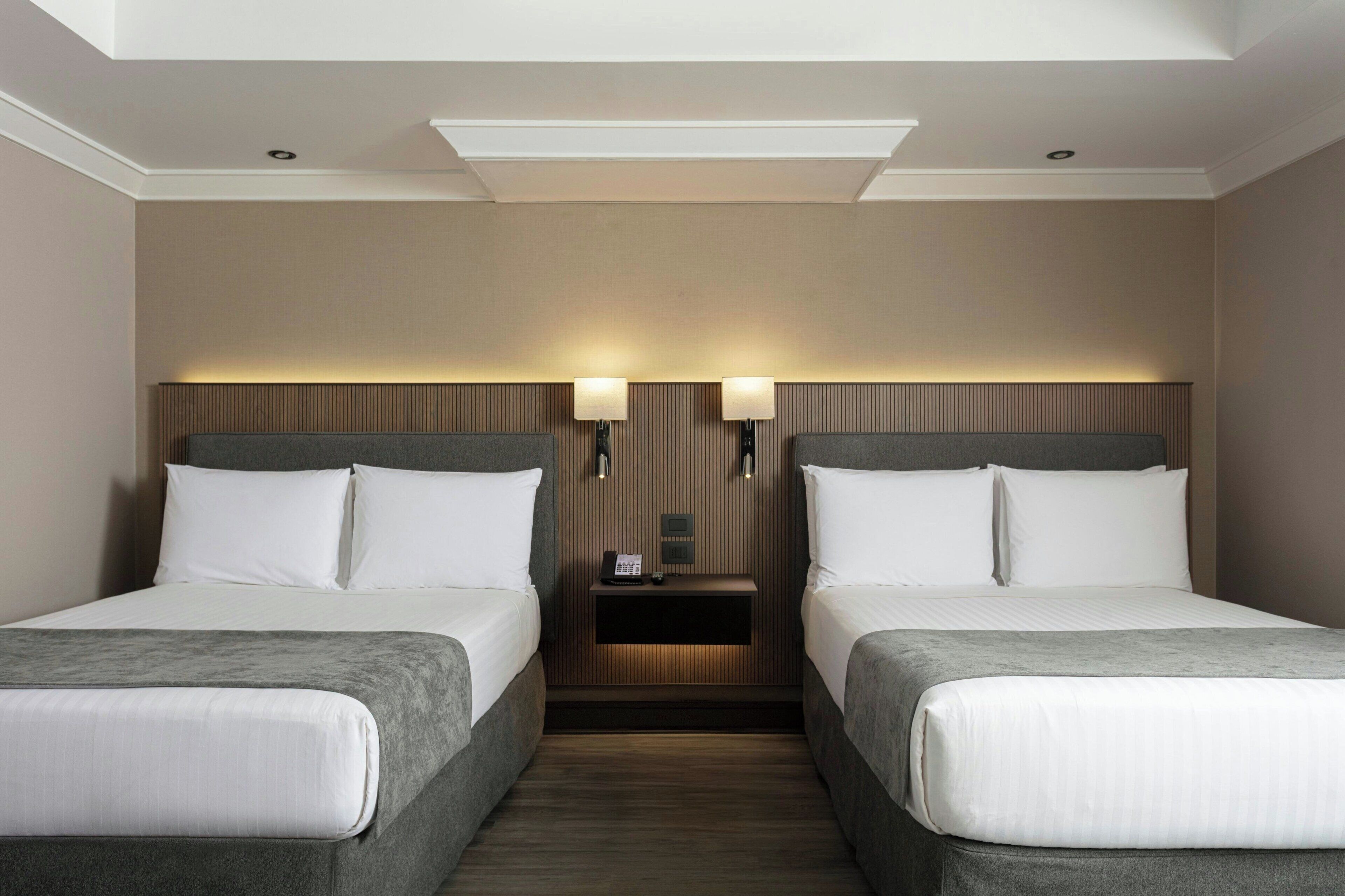 Une chambre d’hôtel avec deux lits, une table de chevet avec une lampe et un téléphone fixé au mur.