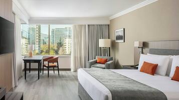 Ein Hotelzimmer mit Bett, Schreibtisch, Stuhl, Lampe und Blick auf die Stadt.