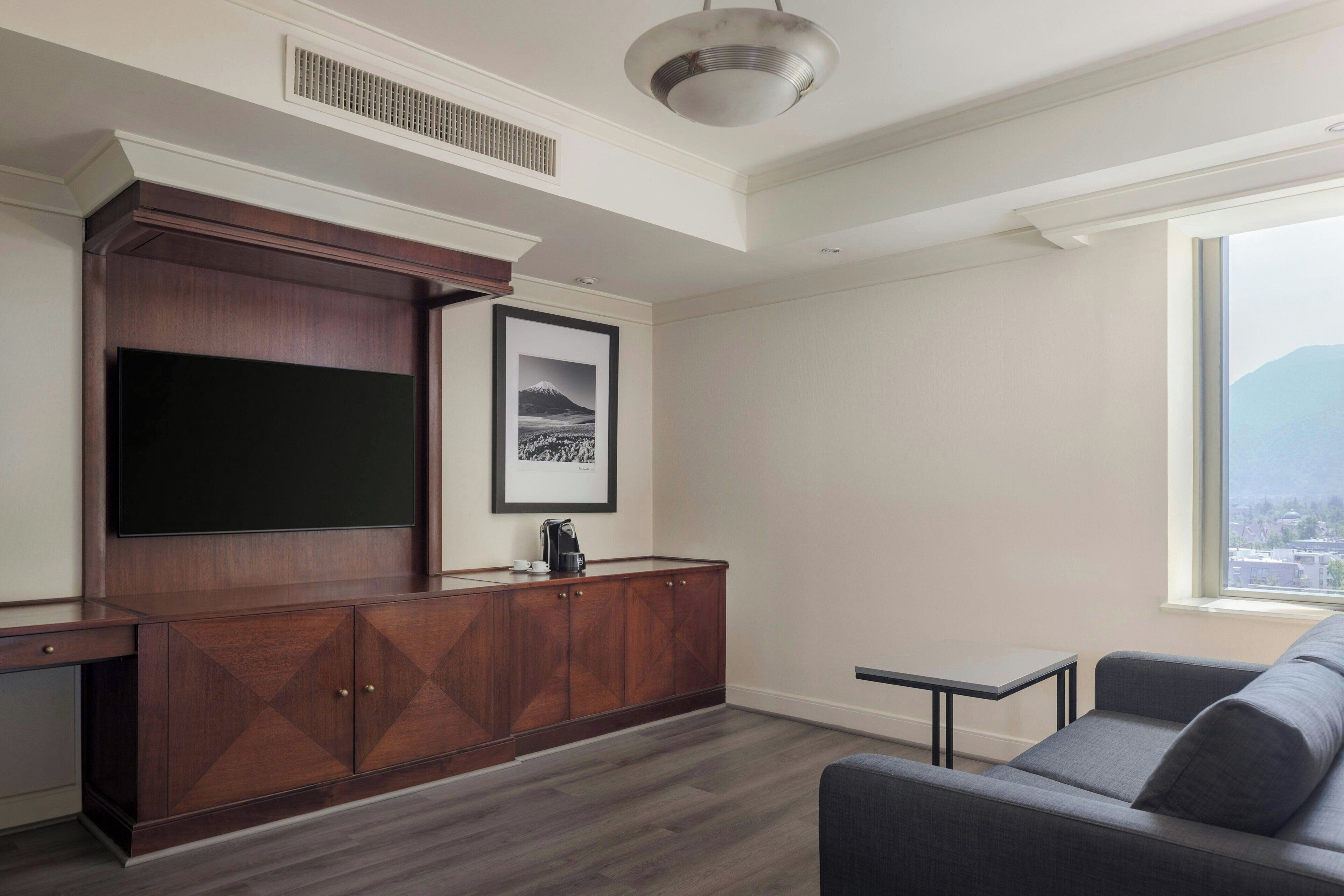 A modern living room with a built-in entertainment unit, a grey sofa, and a large window offering a city view.