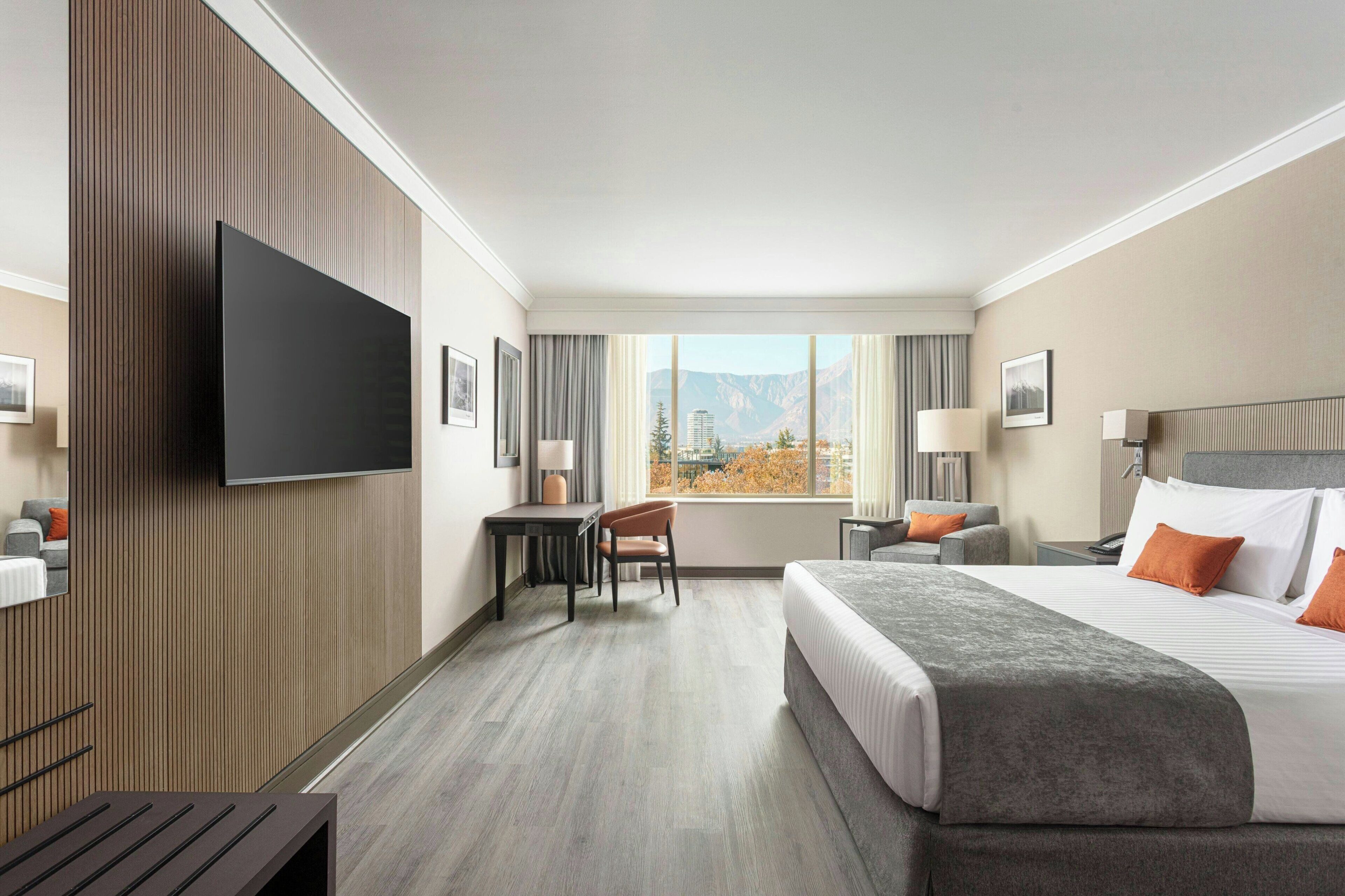 A hotel room with a bed, a desk, a chair, a television, and a window with a mountain view.