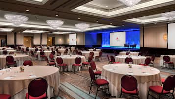 Une salle de conférence dotée de plusieurs tables rondes, de chaises rouges et d’une scène avec un écran de présentation.