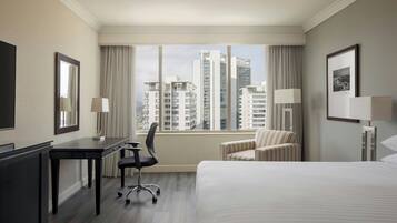 Habitación de hotel con cama, escritorio, silla, televisión y ventana con vista a la ciudad.