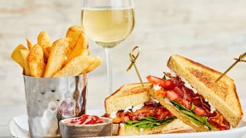 Un sandwich au bacon, à la tomate et à la laitue, un verre de vin blanc et une portion de frites.