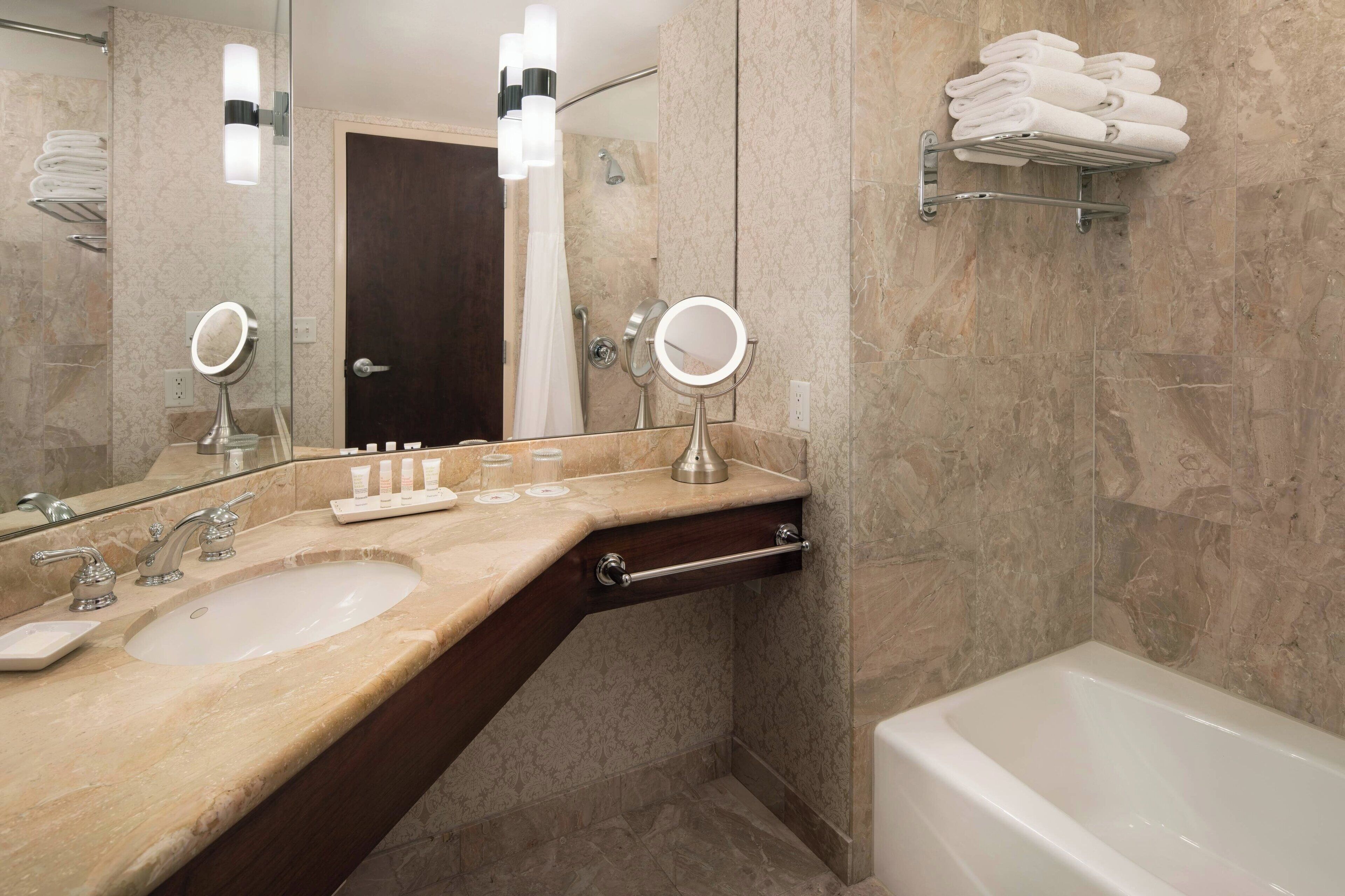 A bathroom with a marble sink, two mirrors, a towel rack, and a bathtub.