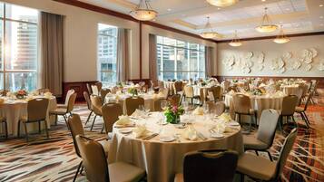 A banquet hall with round tables set for dining, large windows, and a patterned carpet.