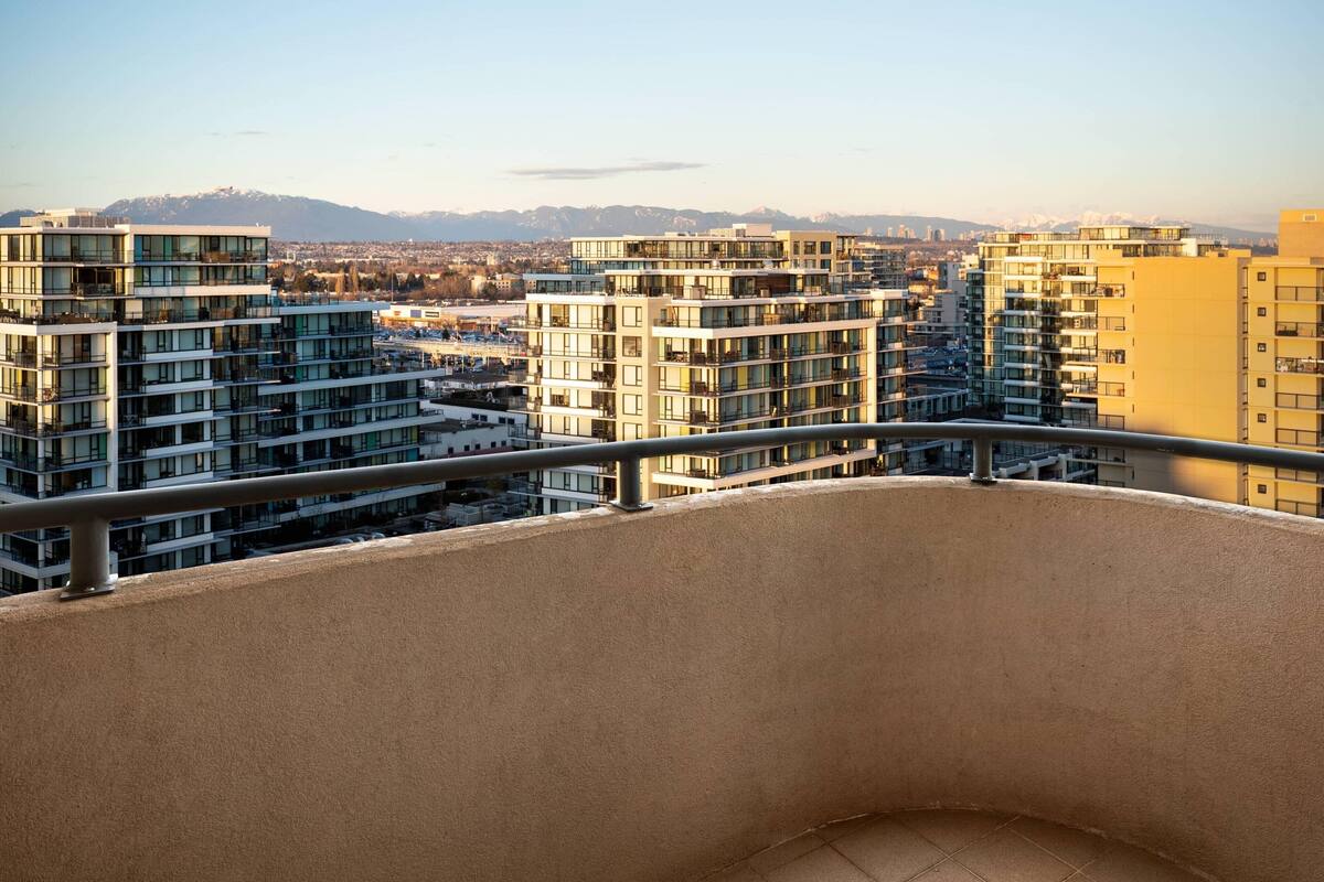 Un edificio residencial de gran altura con varios balcones, ventanas amplias y vistas a un paisaje urbano con montañas al fondo.