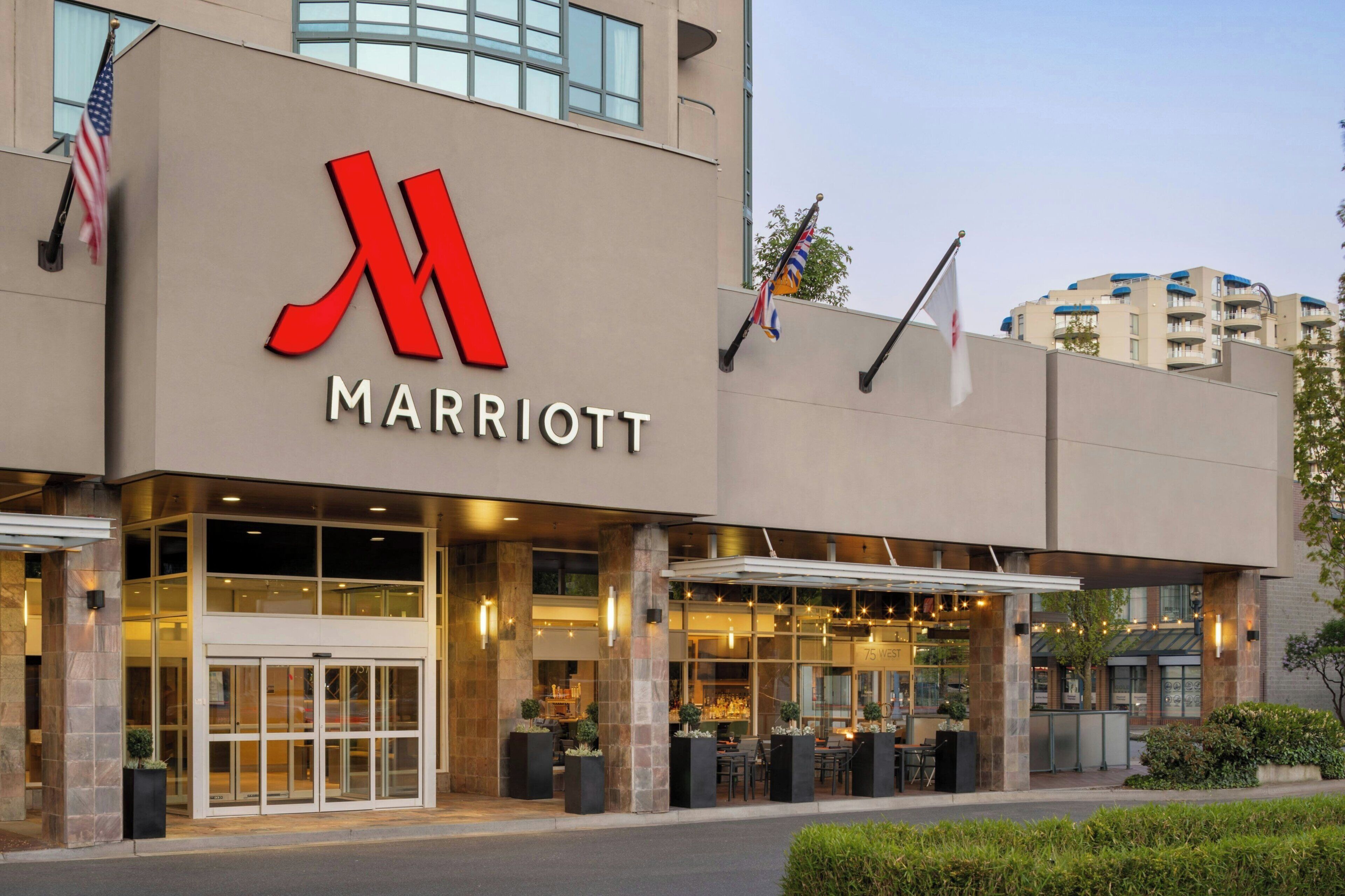 Entrada de un hotel Marriott con un gran logo 'M' rojo, puertas de vidrio y zona de estar al aire libre.