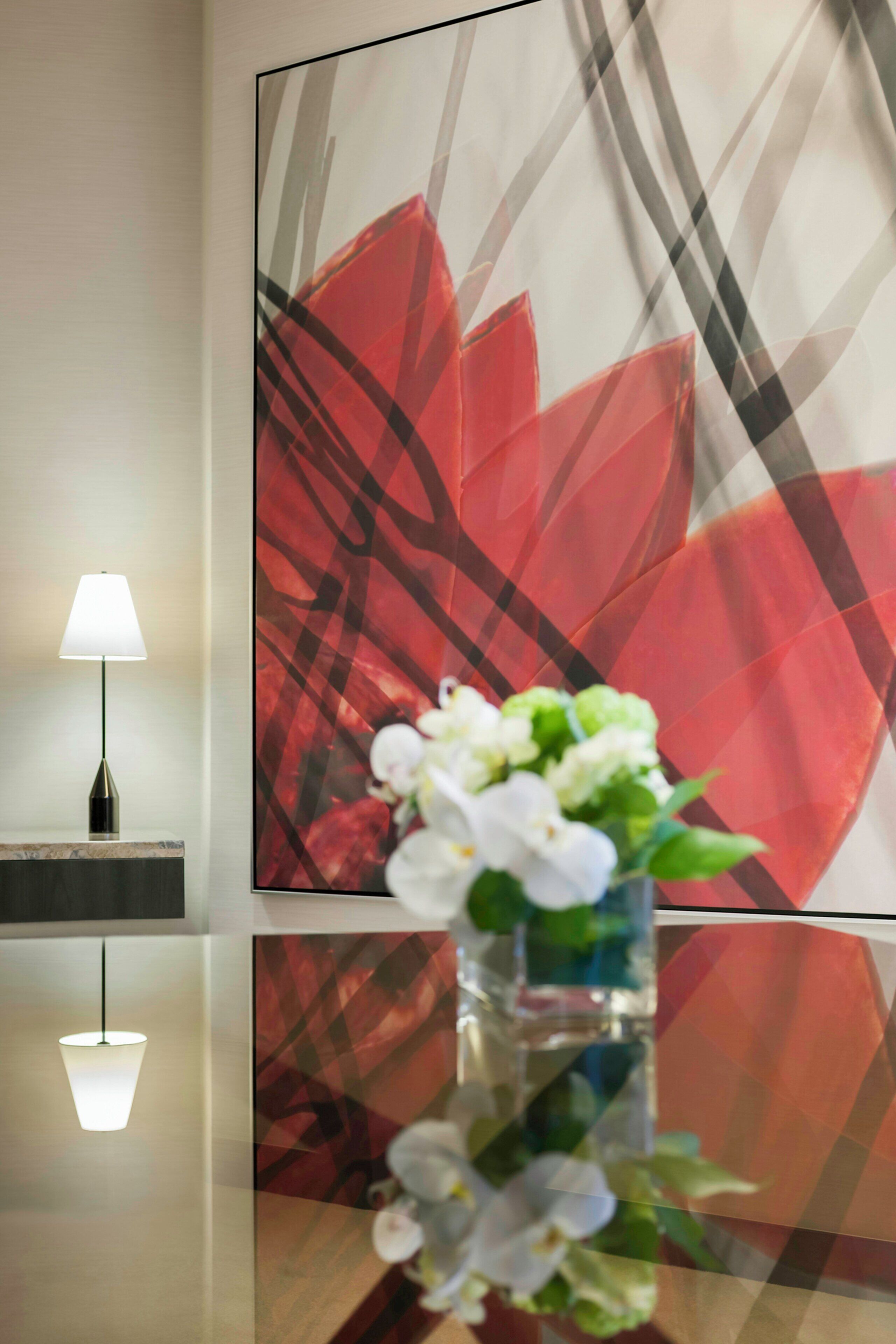 A modern interior with a minimalist lamp, a large abstract painting, and a vase with white flowers on a reflective surface.