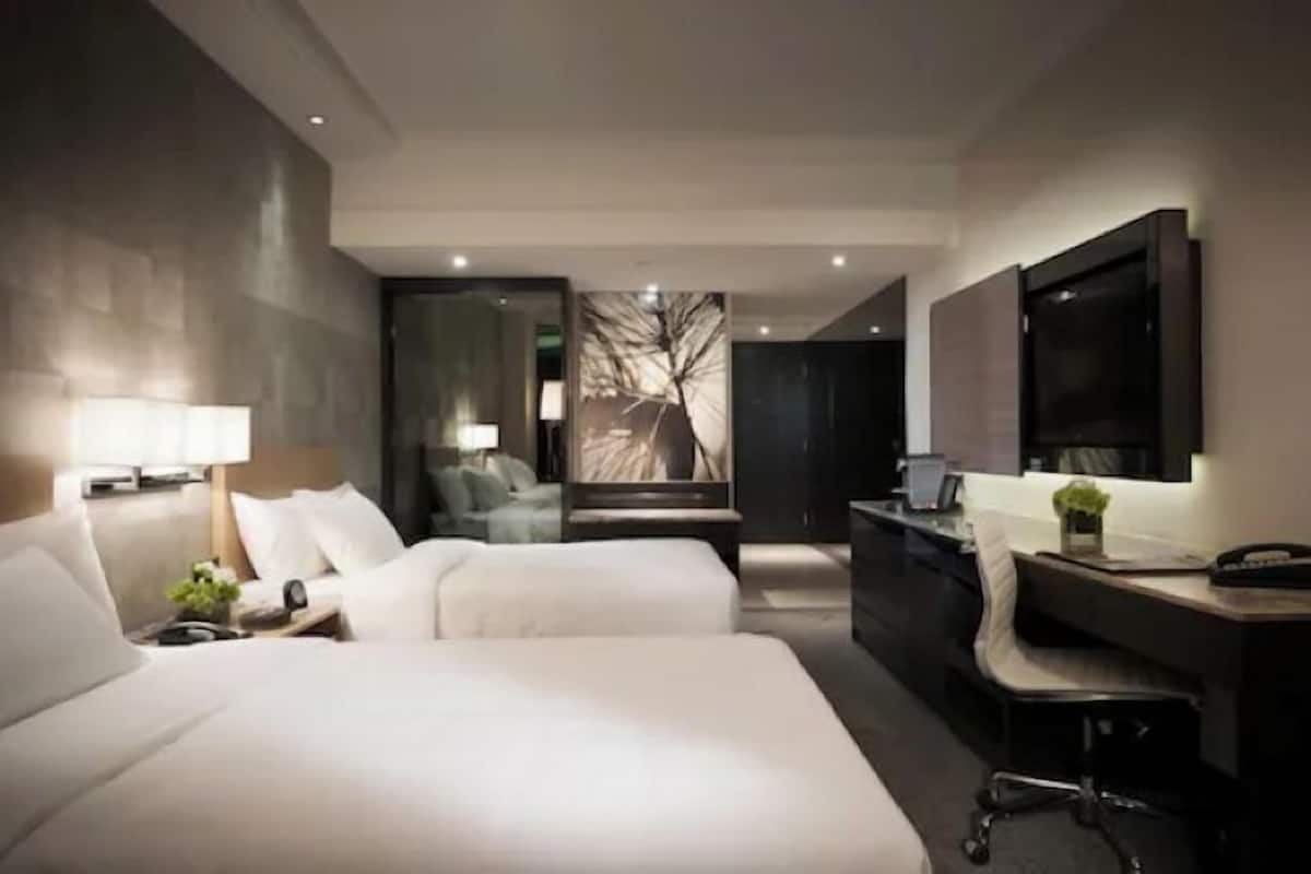 A modern hotel room with two beds, a desk, a chair, and a large mirror.