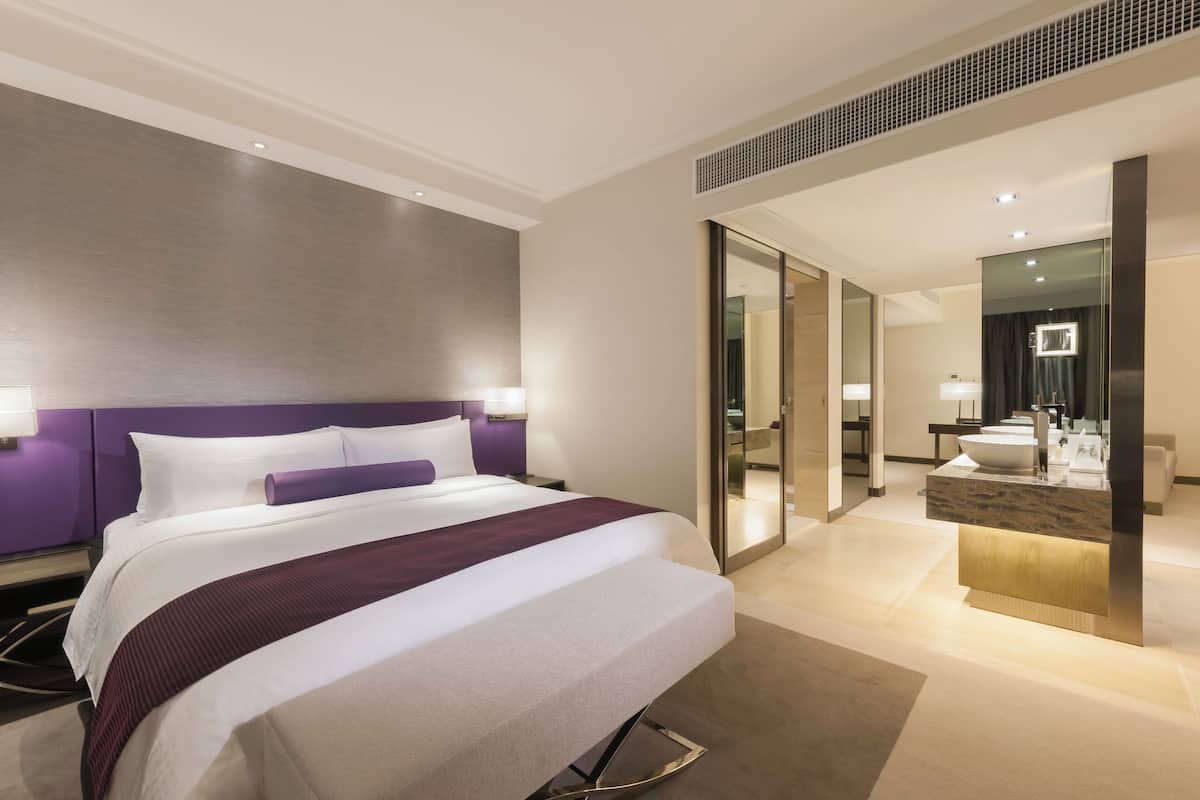 A modern hotel room with a large bed, a bathroom with a vanity, and a large mirror.