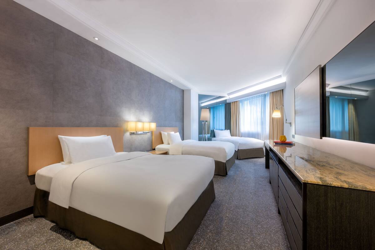 A hotel room with two beds, a large mirror, a dresser, and a view of the city.
