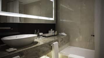 A modern bathroom with a large oval sink, a mirror, a bathtub, and a vanity with toiletries.