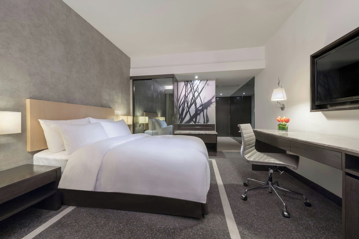 A hotel room with a bed, bedside tables, a desk, a chair, a TV, and a window with a view.