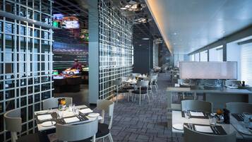 Een modern restaurant met een rastervormige plafondconstructie, tafels met stoelen en uitzicht door grote ramen.