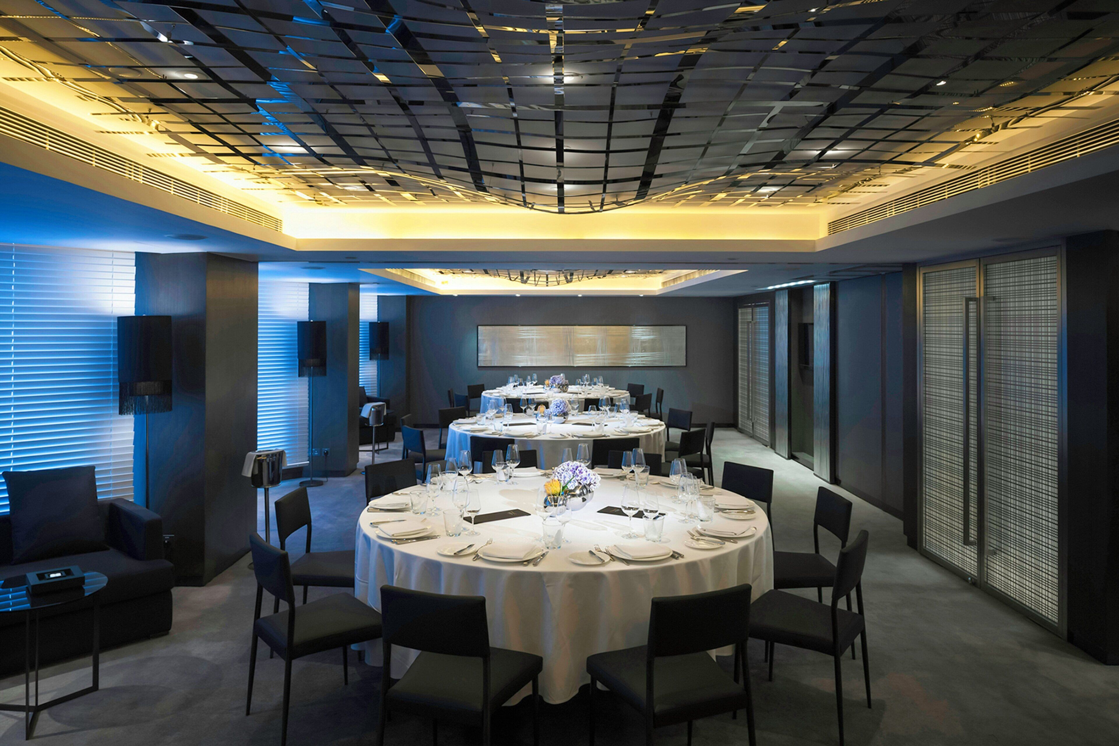 A modern dining area with round tables set for a meal, featuring a geometric ceiling design and large windows.
