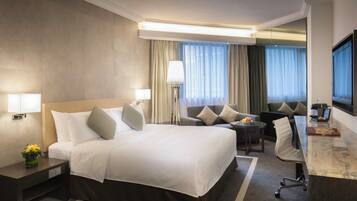 A hotel room with a large bed, a desk, a chair, a lamp, and a TV.
