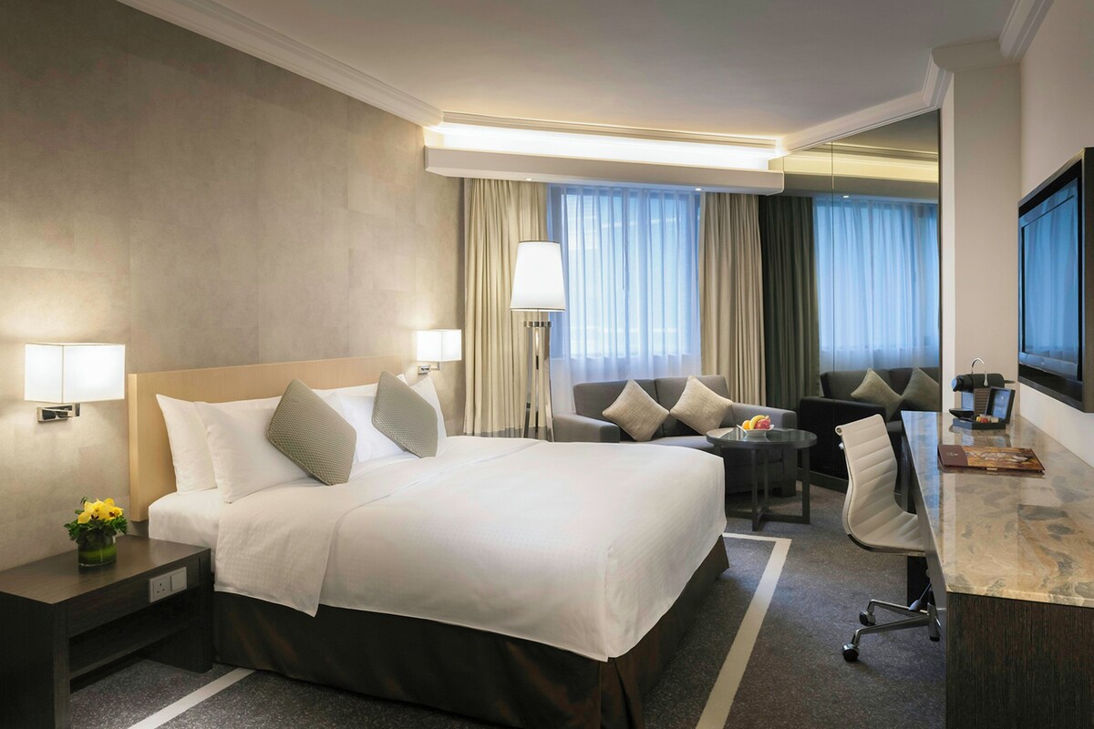 A hotel room with a bed, bedside tables, a desk, a chair, a lamp, and a TV.
