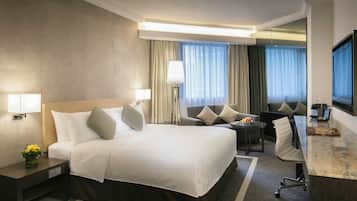 A hotel room with a bed, bedside tables, a desk, a chair, a lamp, and a TV.
