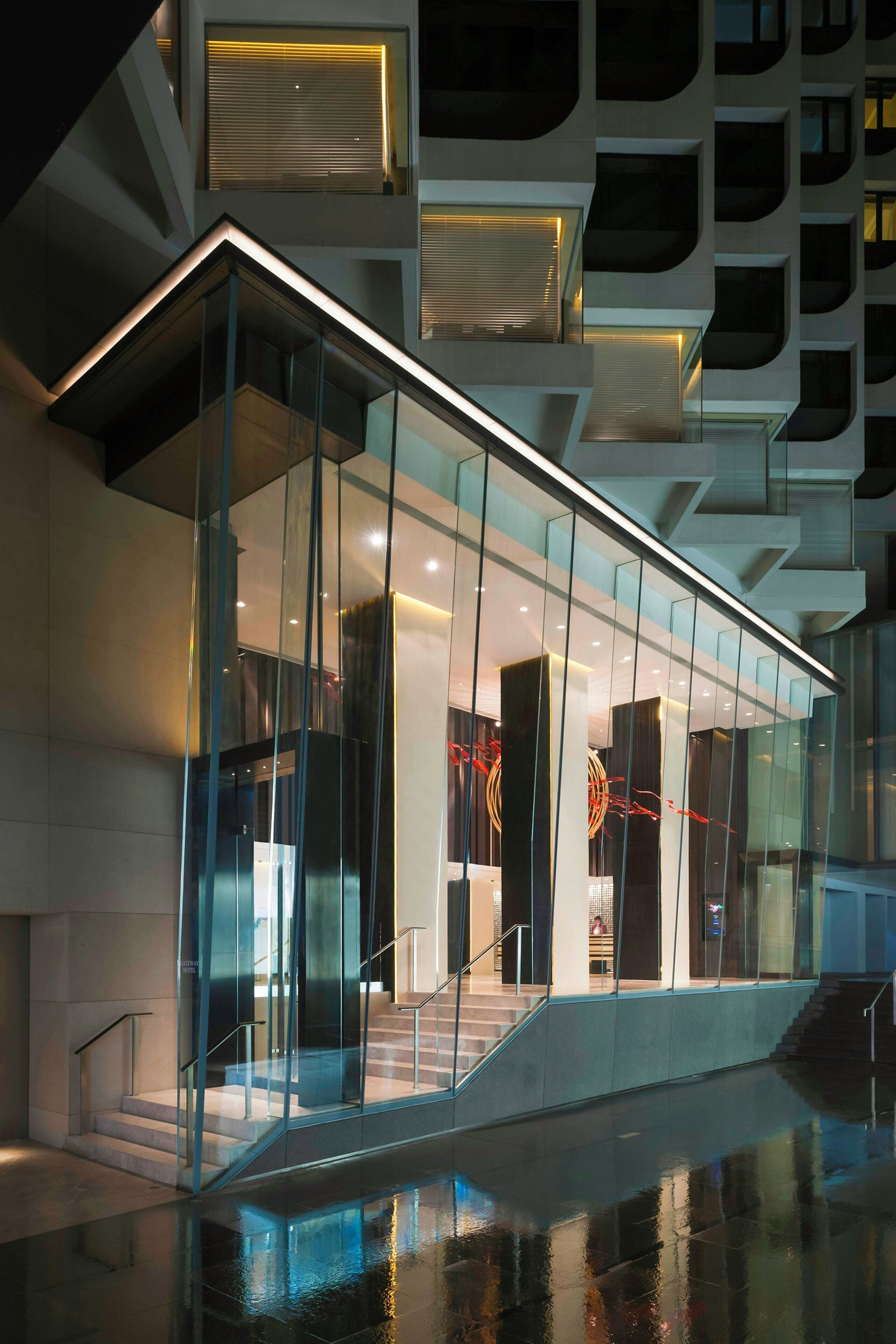A modern building with a glass facade, a staircase leading to an upper level, and a pool area in the foreground.