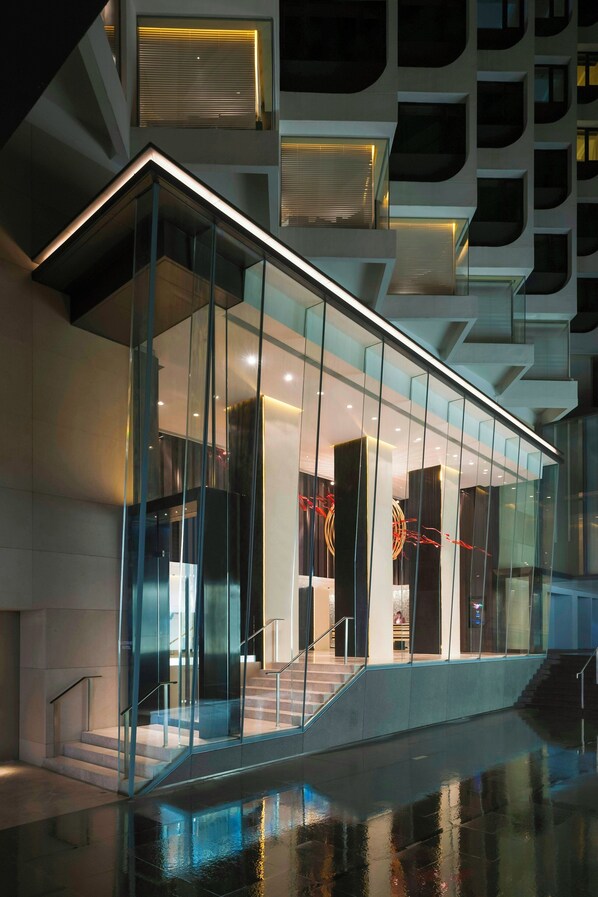 A modern building with a glass facade, a staircase leading to an upper level, and a pool area in the foreground.