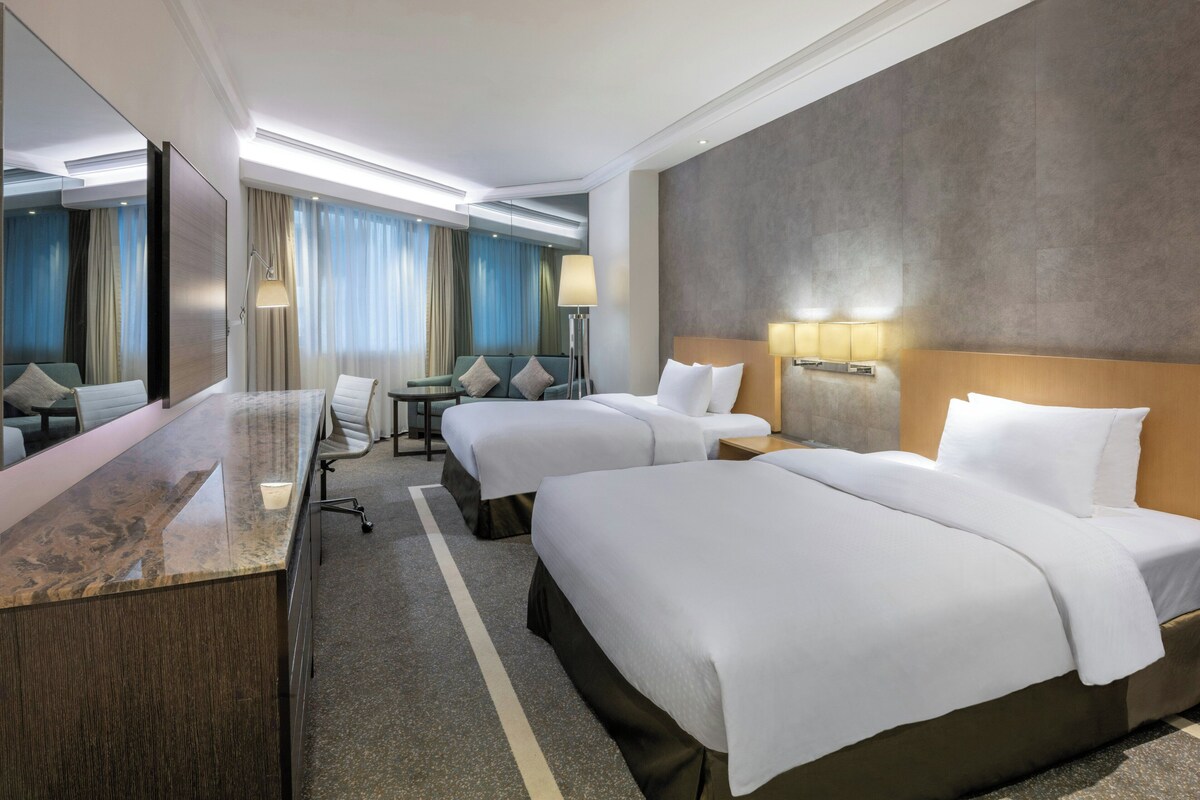 A hotel room with two beds, a desk, a chair, and a large mirror.
