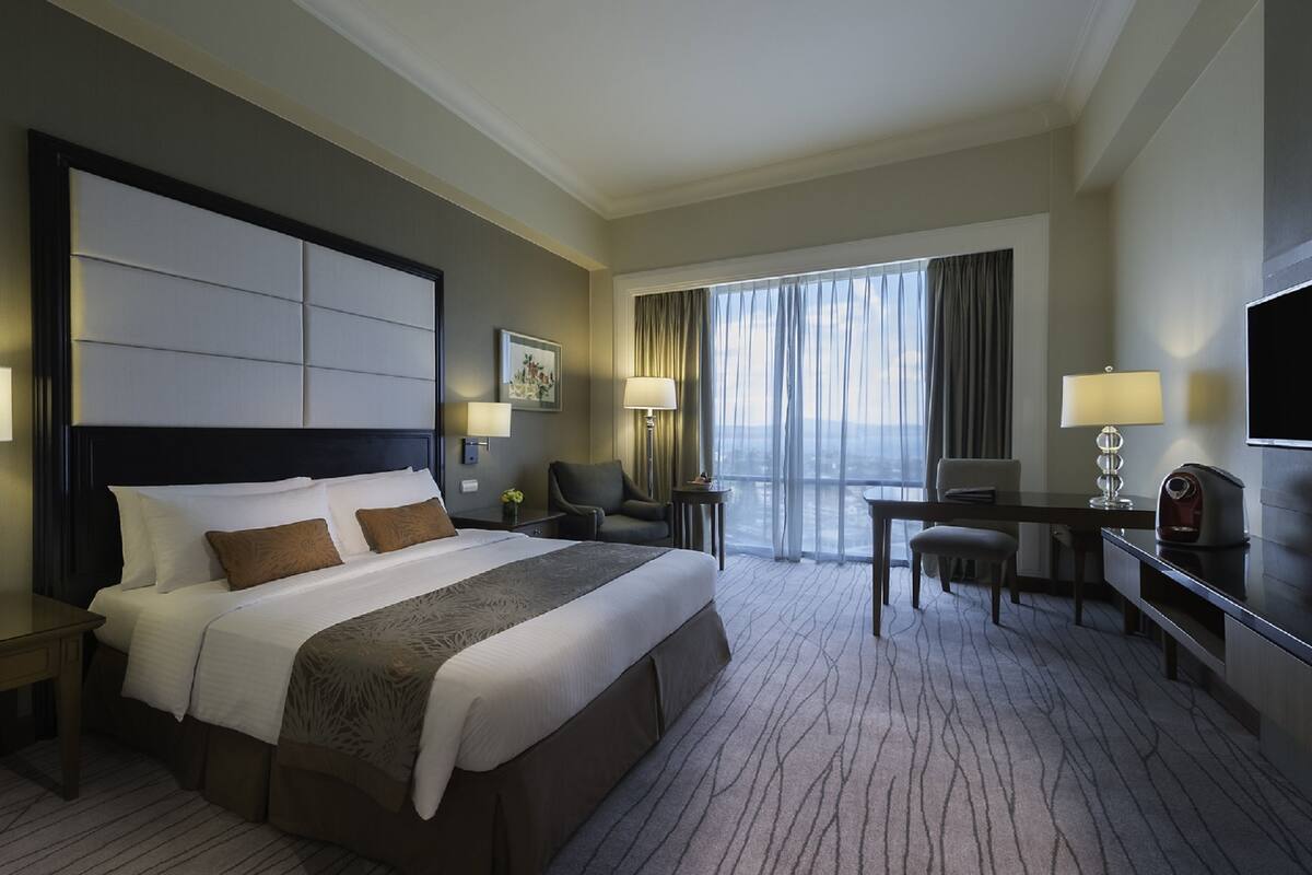 Quarto de hotel com uma cama grande, uma escrivaninha, uma cadeira, uma televisão e vista para o exterior.