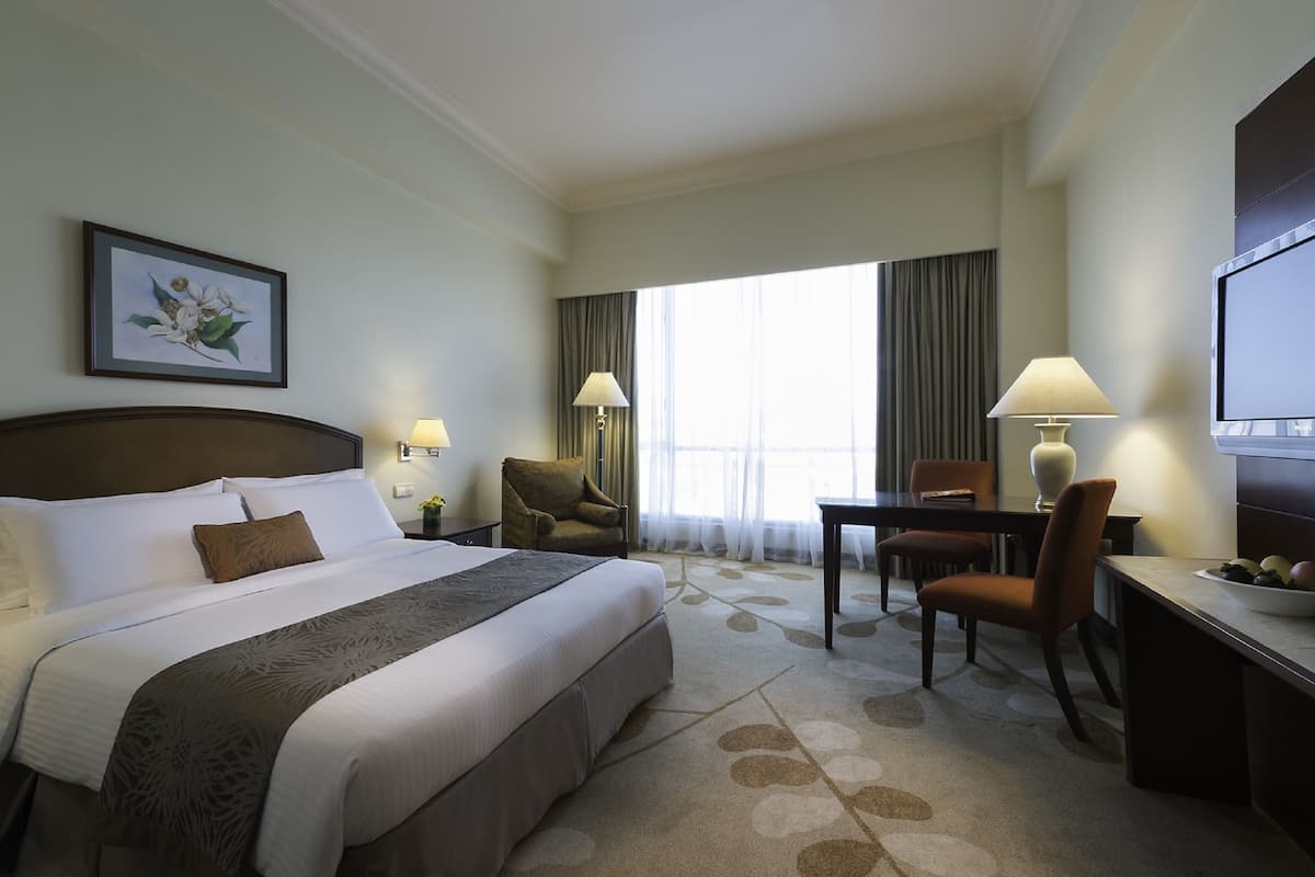 Quarto de hotel com uma cama grande, uma escrivaninha com cadeira, televisão e janela com cortinas.