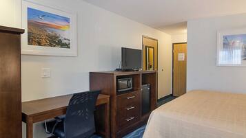 A hotel room with a desk, chair, bed, and a television.