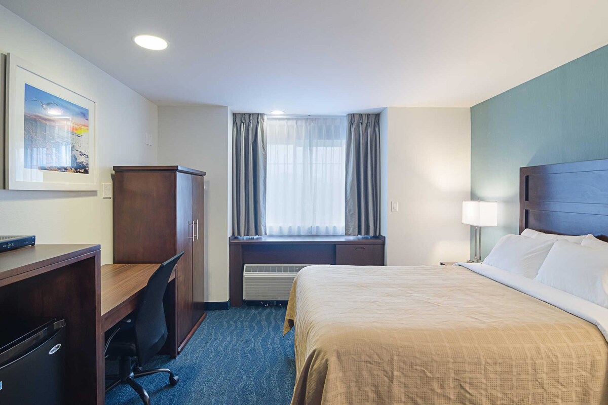 Habitación de hotel con cama, escritorio, silla y ventana con cortinas.