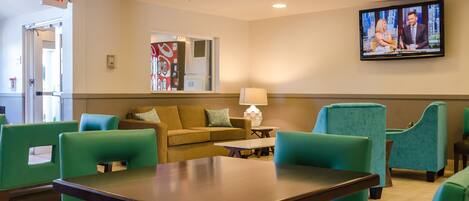 A hotel lobby with green chairs, a sofa, a TV on the wall, and an exit sign.