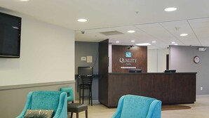 A reception area with a wooden desk, two teal chairs, and a clock on the wall.