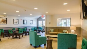 A spacious room with green upholstered chairs and tables, a sofa, and a window providing natural light.