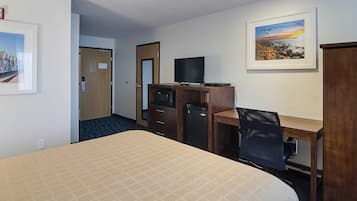 Habitación de hotel con cama, escritorio con computadora, televisor y refrigerador pequeño.