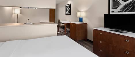 A hotel room with a bed, a desk, a chair, a TV, a lamp, and a framed picture on the wall.