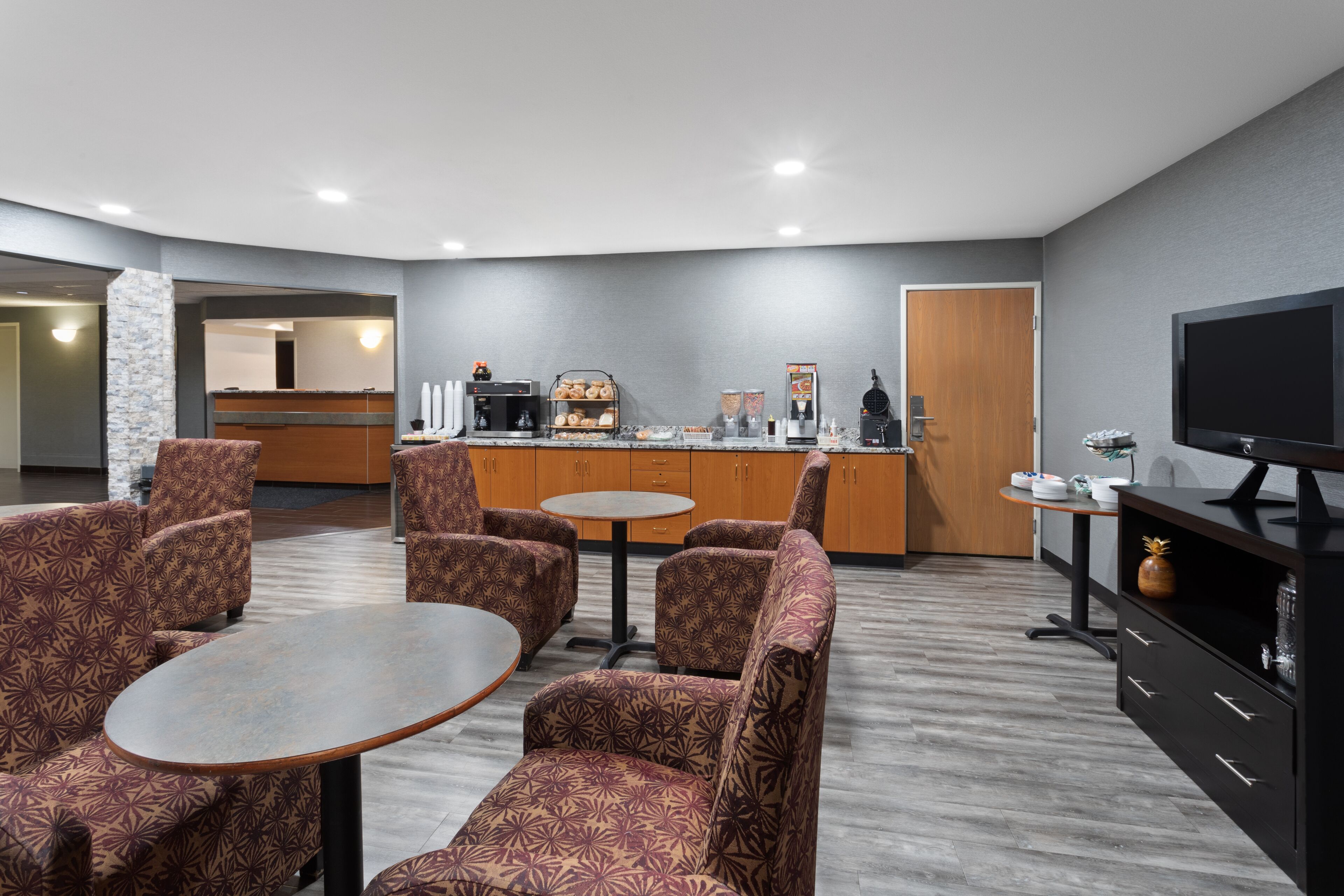 Eine moderne Hotelhalle mit gemusterten Sitzgelegenheiten, einer Kaffeestation, einem Fernseher und einer Rezeption.