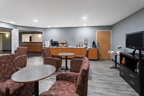 A modern hotel lobby with patterned seating, a coffee station, a TV, and a reception area.