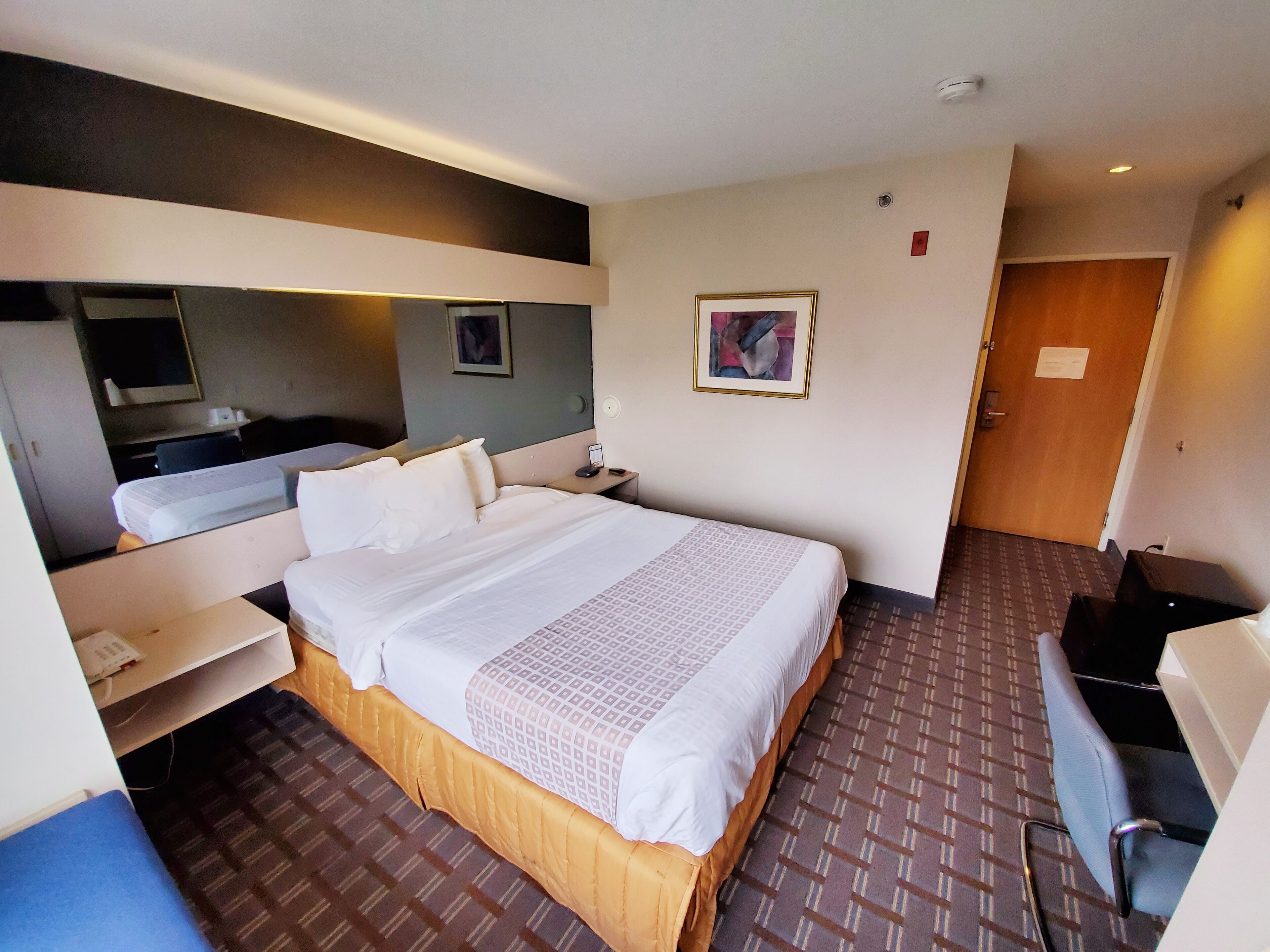Une chambre d’hôtel avec un grand lit, un bureau, une chaise, un miroir et une porte.