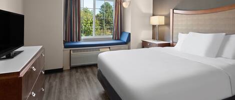 A hotel room with a large bed, a television on a dresser, a window with curtains, and a view of trees.