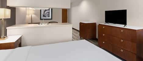 A modern hotel room with a large bed, a wooden dresser, a flat-screen TV, a desk with a lamp, and a framed picture on the wall.