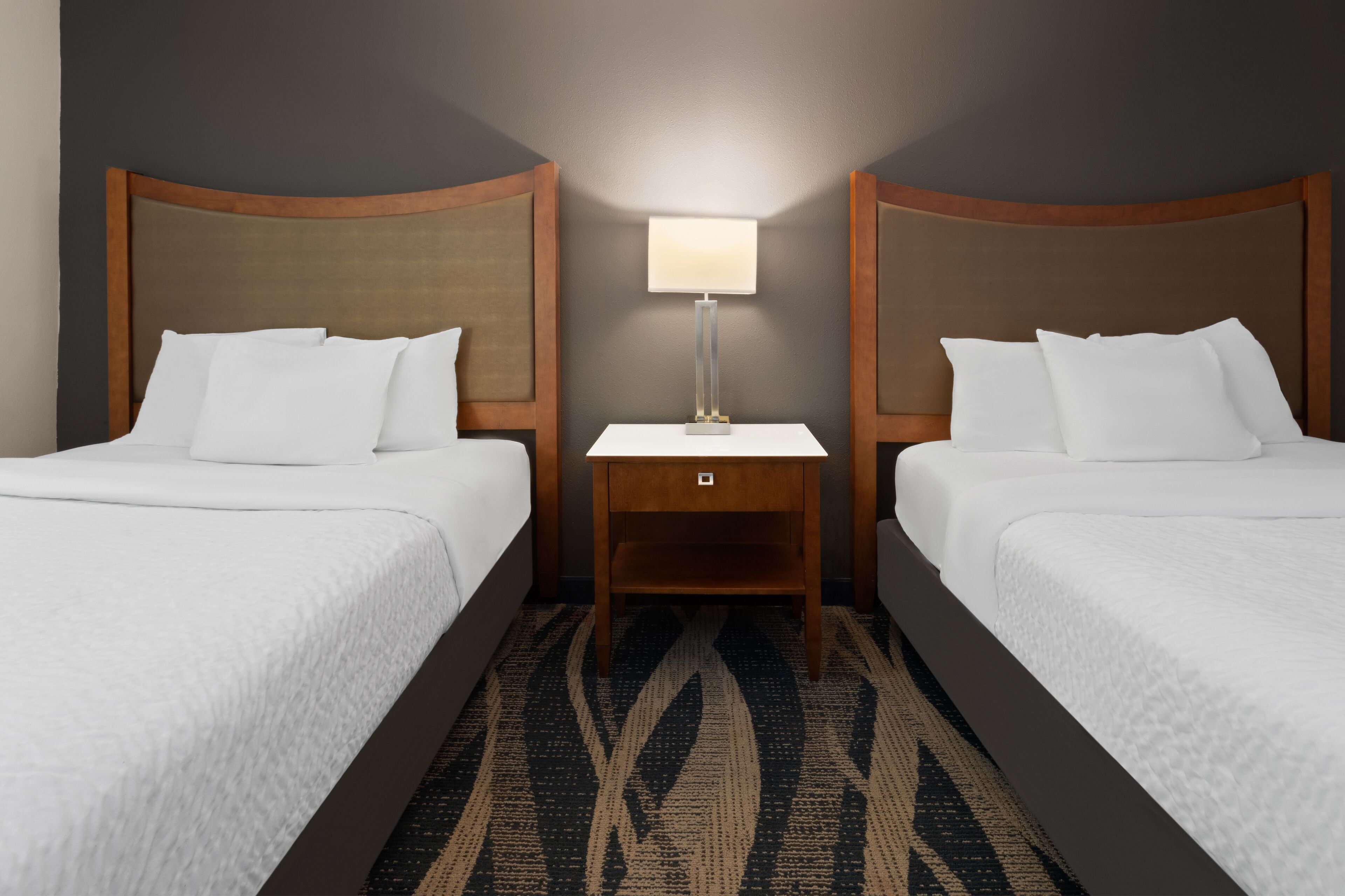 A hotel room with two beds, a nightstand with a lamp, and a patterned carpet.